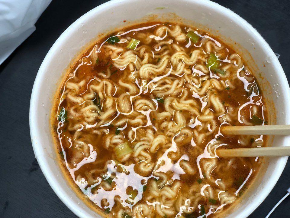 A partially eaten bowl of Omori Kimchi Jjigae Ramen using chopsticks, showcasing the rich soup base and texture.